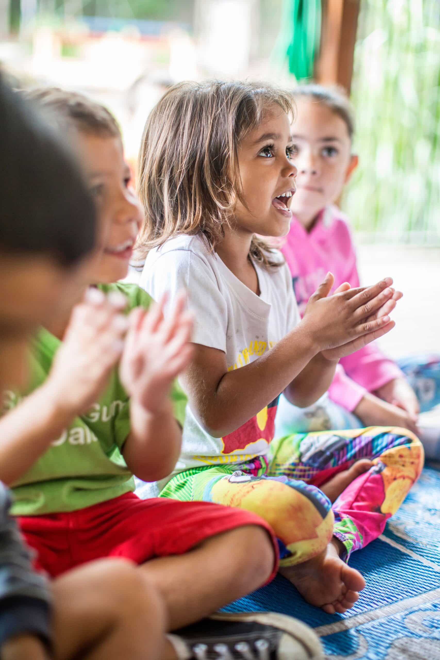 A group of children sitting on the ground, clapping and smiling